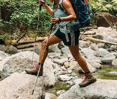 woman hiking over stream walking on rocks