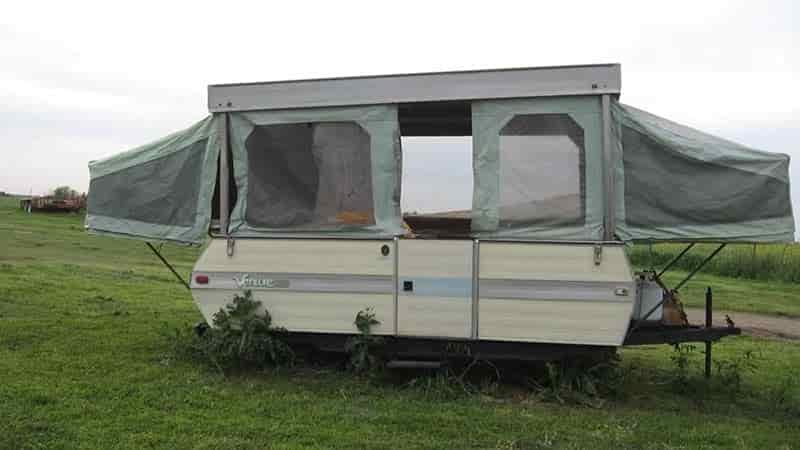 Pop up camper sitting in yard grass growing under camper