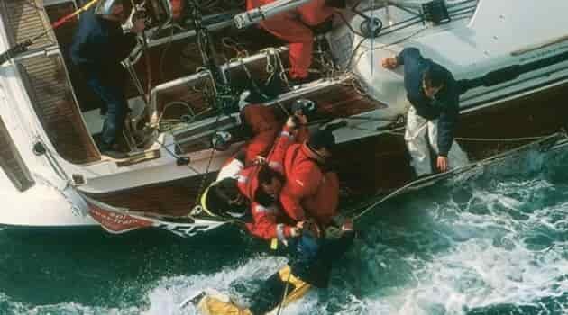 men saving an overboard man on sailboat throwing a line while the boat is on tilt
