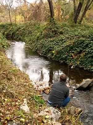 man fishing in small creek sitting down on bank