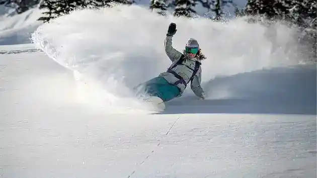 woman snowboarding in fresh powder cutting right hand in snow