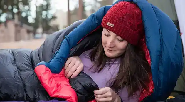 young woman looking at phone wrapped up in sleeping bag