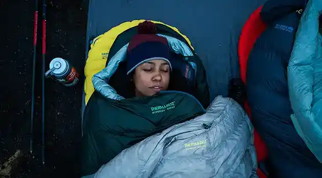 woman sleeping in cozy sleeping bag snow walking poles next to her