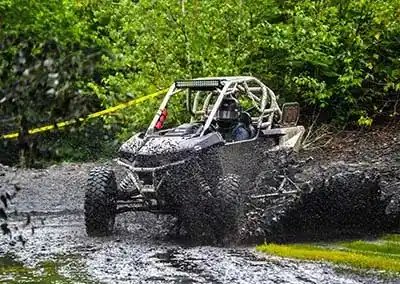 side by side treversing through a muddy wet trail splashing mud and water over the roof