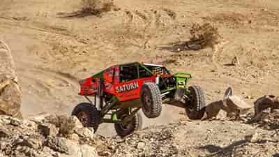 off road race saturn car approacing large boulders in desert race front wheels in the air back wheels spinning in loose dirt