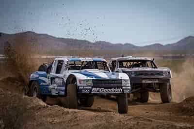 hard off road racing 2 trucks side by side trying to overtake each other while turn in dirt flying