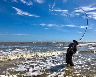 man surf fishing with rod bent over catching a large fish beautiful sunny day