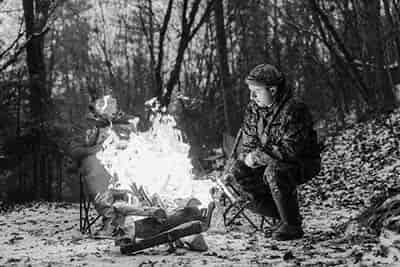 2 men around camp fire warming after afternoon hunt ethics of the chase 1 man loading firewood on flames