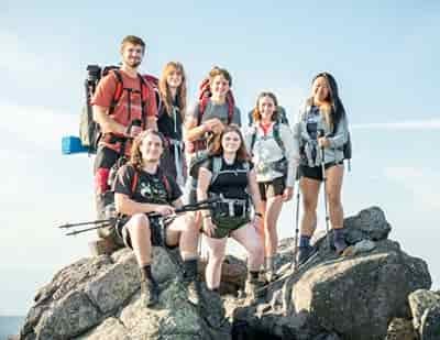 7 college students taking meme on top of rock formation in mountains hiking