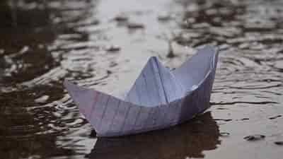 notebook paper boat in rain floating down street gutter