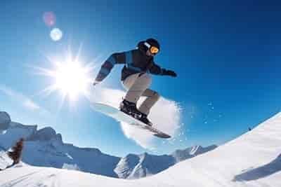 Jumping snowboarder young man sun in background