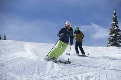 man and woman skiing on groomed slope at an average speed with helmets