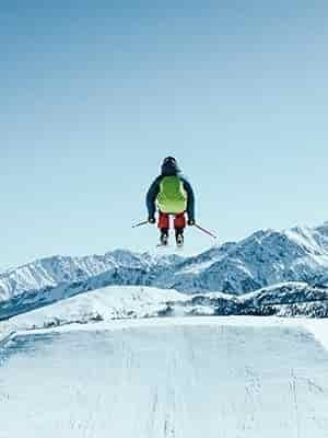 man ski jumping groomed hill overlooking mountain range