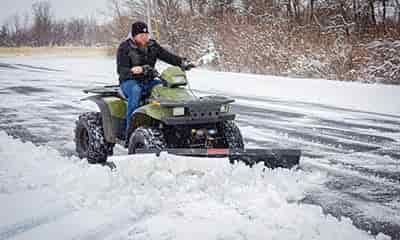 man plowing snow on atv from roadway