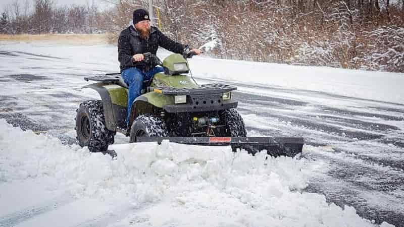 man on atv plowing snow from roadway