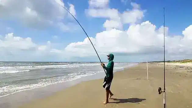 man beach fishing with hoodie on and 3 poles